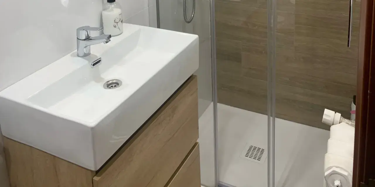 Lavabo moderno con mueble de madera y ducha acristalada. Un ejemplo de cuartos de baño modernos y funcionales.