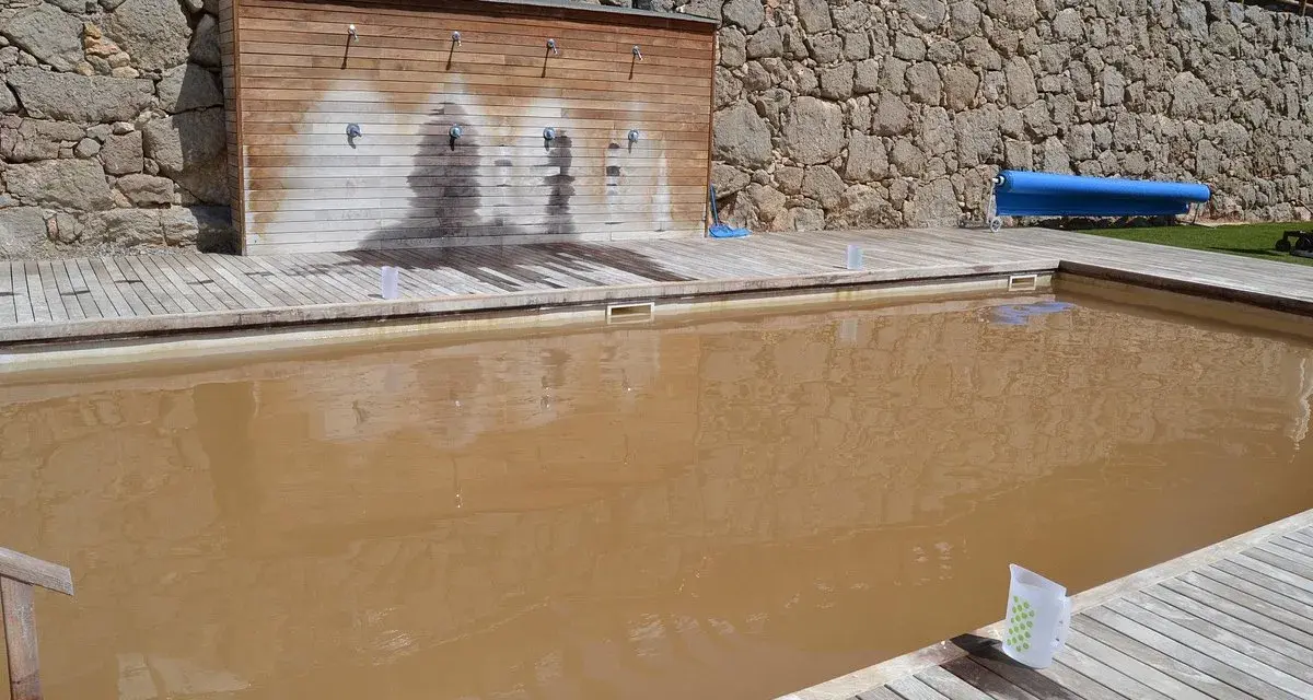 Una piscina de agua salada con un revestimiento de madera y duchas. El agua es de color marrón turbio.