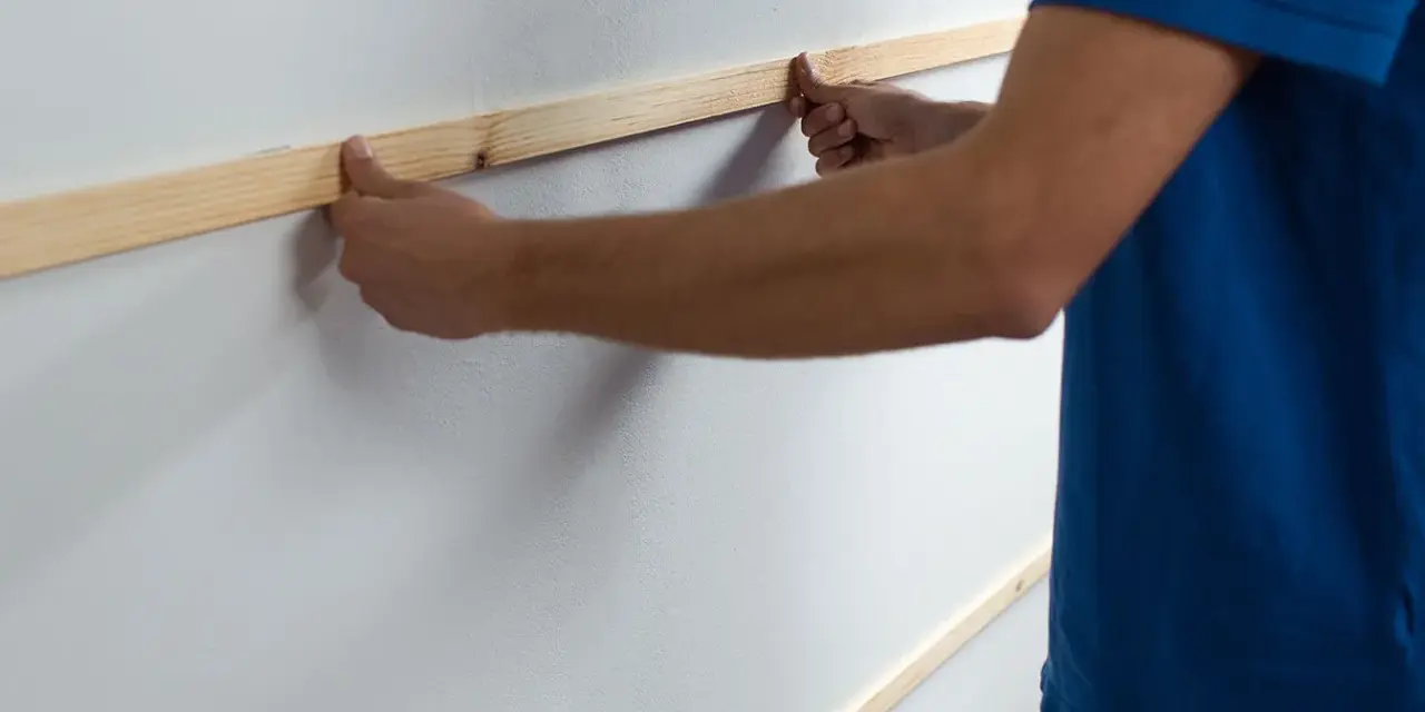 Man placing wooden slats on a white wall, demonstrating como poner listones de madera en la pared.