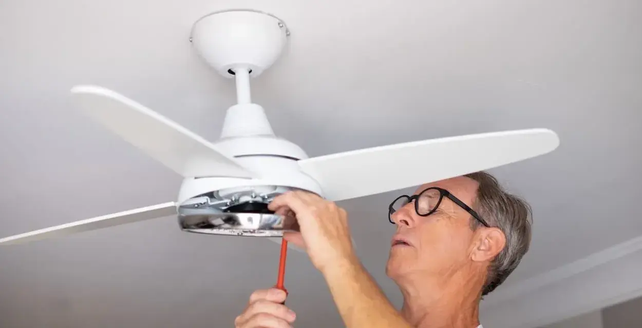 Hombre con gafas ajusta un ventilador de techo pladur con un destornillador.