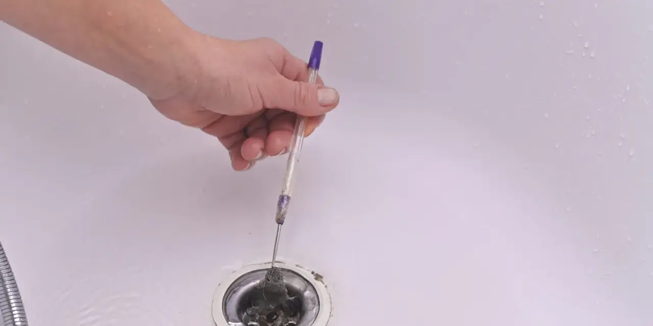 Mano usando un bolígrafo para quitar pelo y desatascar la ducha.