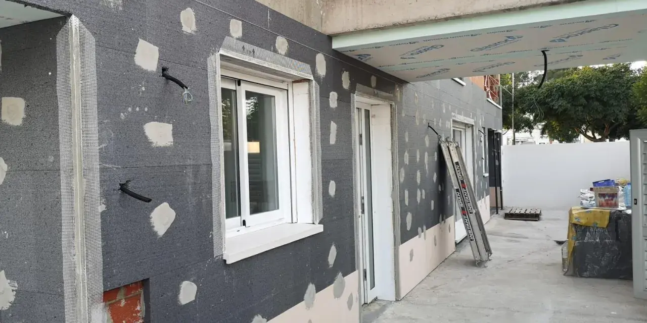 Fachada en construcción con aislamiento SATE, tuberías y ventanas.