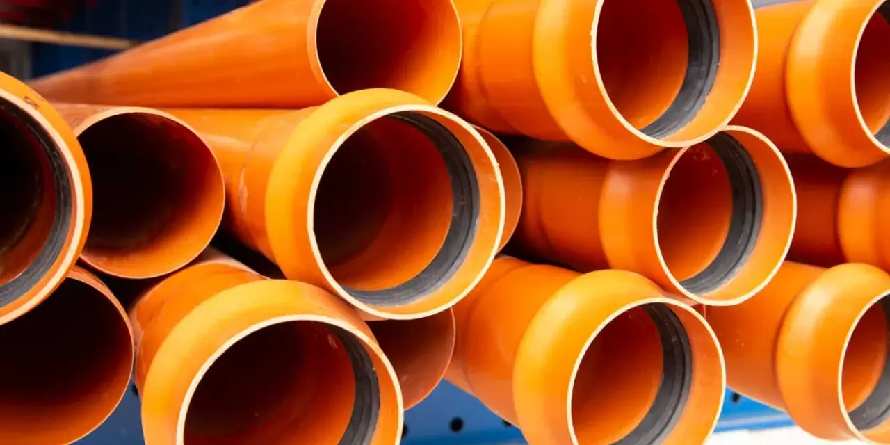 Tubos de PVC naranja apilados, listos para ser instalados en exteriores. Perfectos para proyectos de fontanería y drenaje.