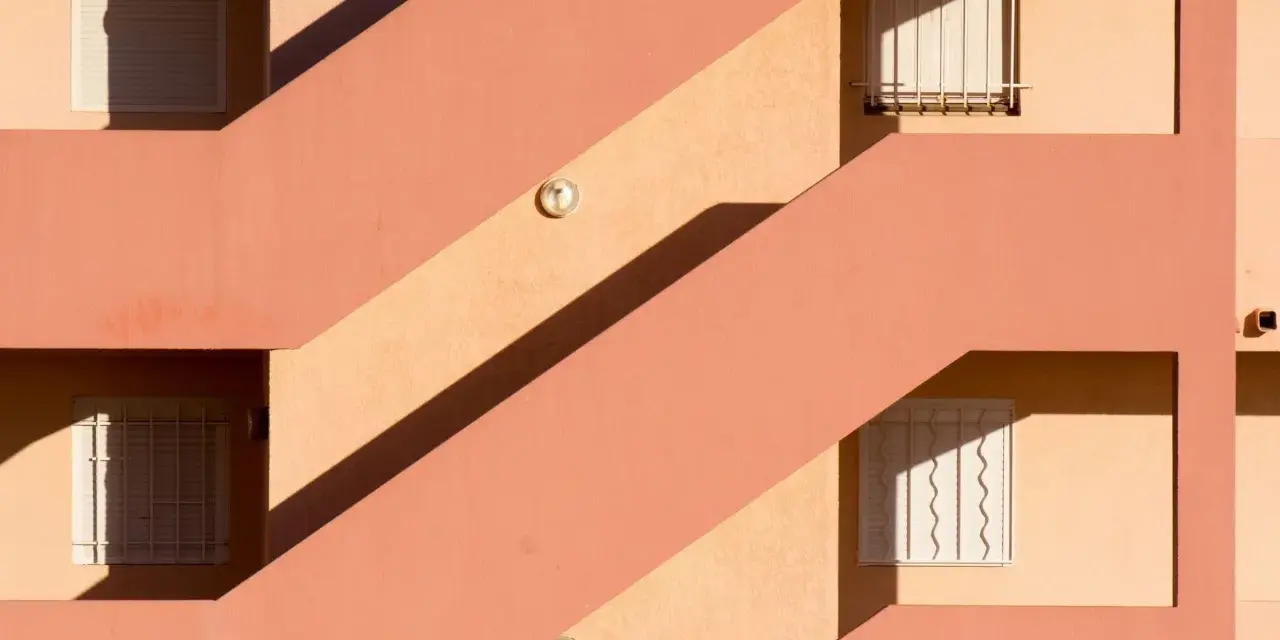 Fachada con escaleras y ventanas, sombras marcadas. Un ejemplo de cómo impermeabilizar pared exterior para protegerla.