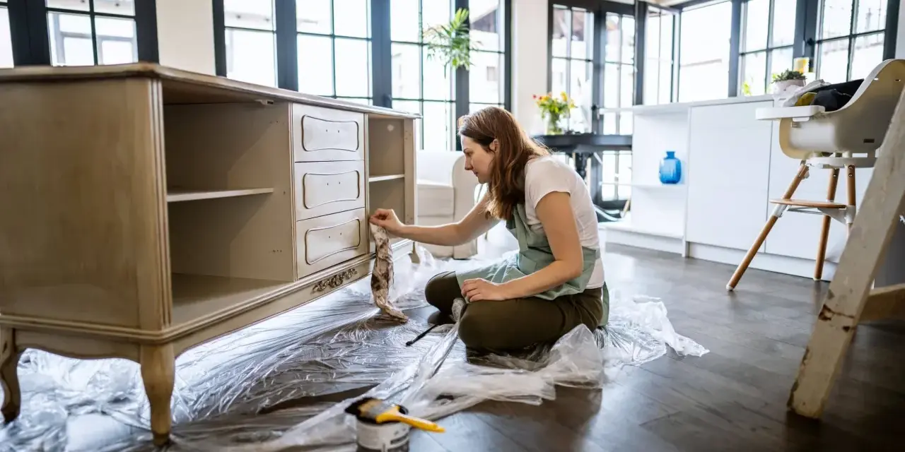 Mujer aplicando una capa de pintura a un mueble antiguo.