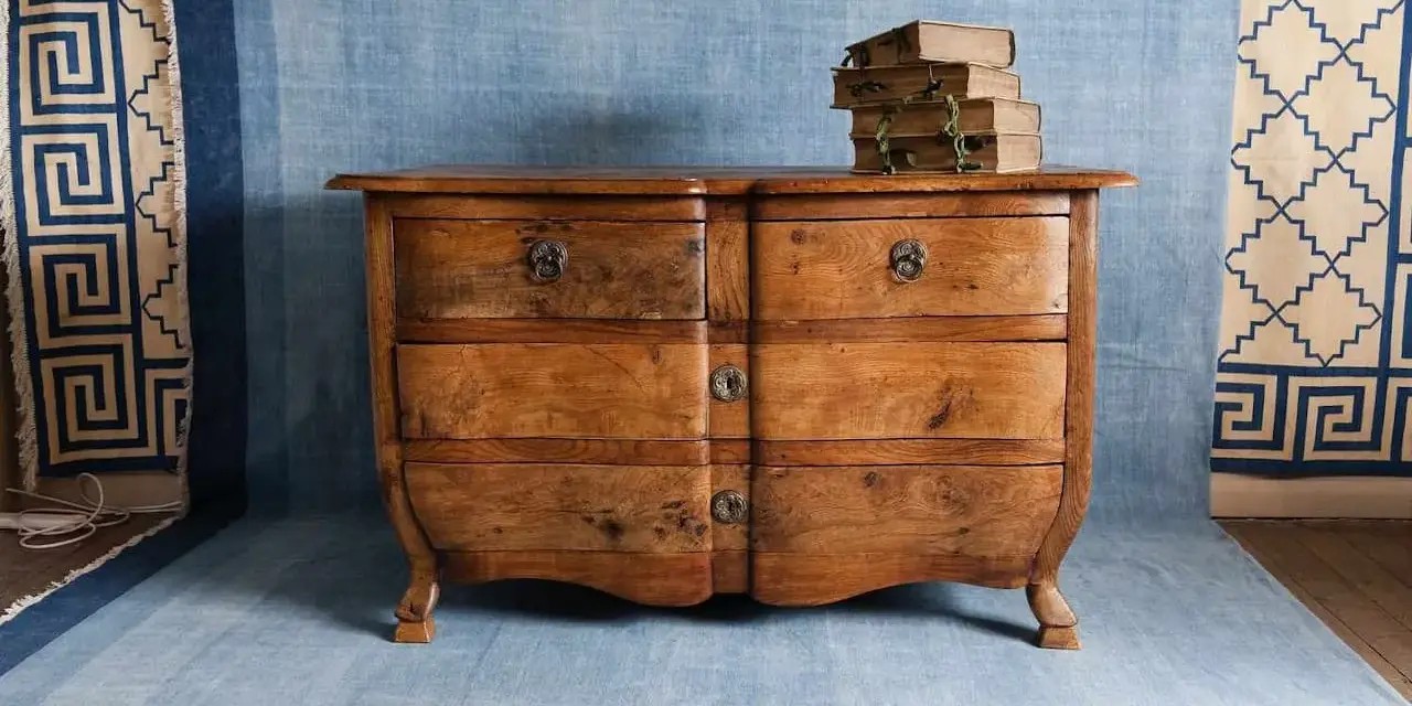 Cómoda de madera antigua, lista para pintar. Unos libros apilados descansan sobre ella.