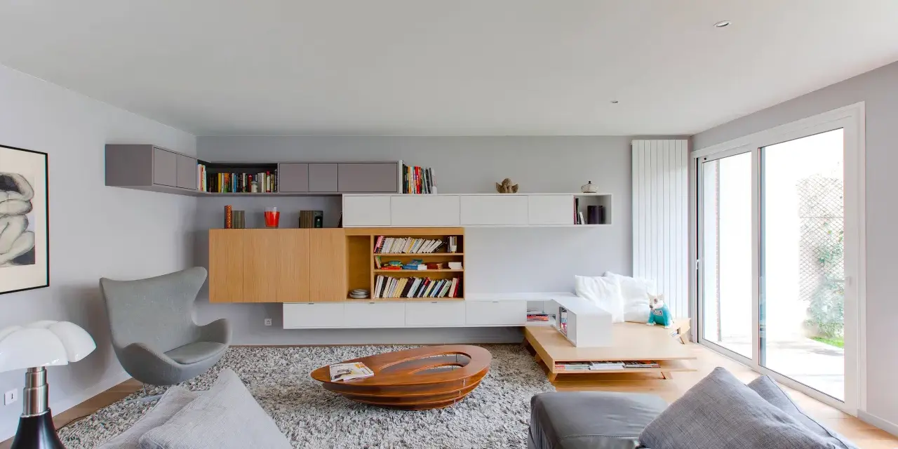 Salón moderno con estanterías empotradas y una **color crema pared**. Sofá de cuero, sillón gris y mesa de centro ovalada.