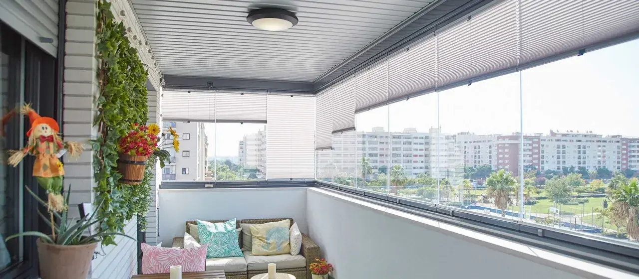 Ideas para tapar balcón: un espacio acogedor con sofá, plantas y vistas urbanas.