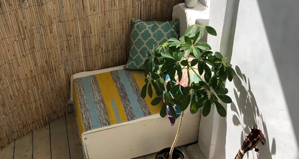Un rincón acogedor para decorar balcon. Un banco con cojines, planta y luces crea un ambiente relajado.