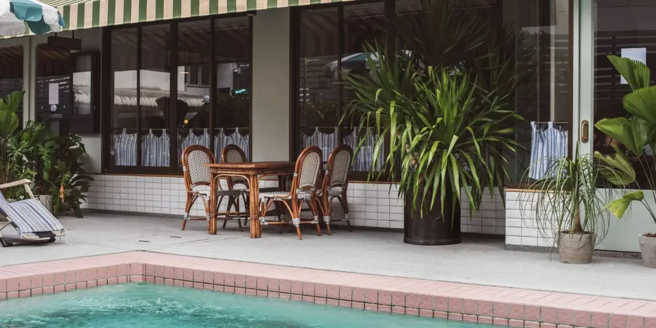 Terraza con piscina y toldo a rayas verdes y blancas. Mesa de madera con sillas de mimbre listas para instalar toldo.