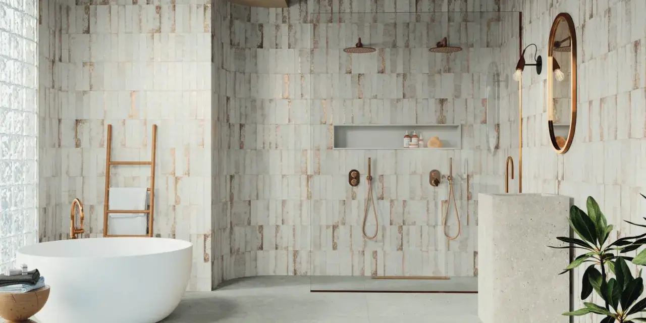 Baño moderno con bañera exenta y ducha doble. Las paredes presentan azulejos con un diseño rústico y detalles dorados, reflejando las últimas tendencias azulejos baño.