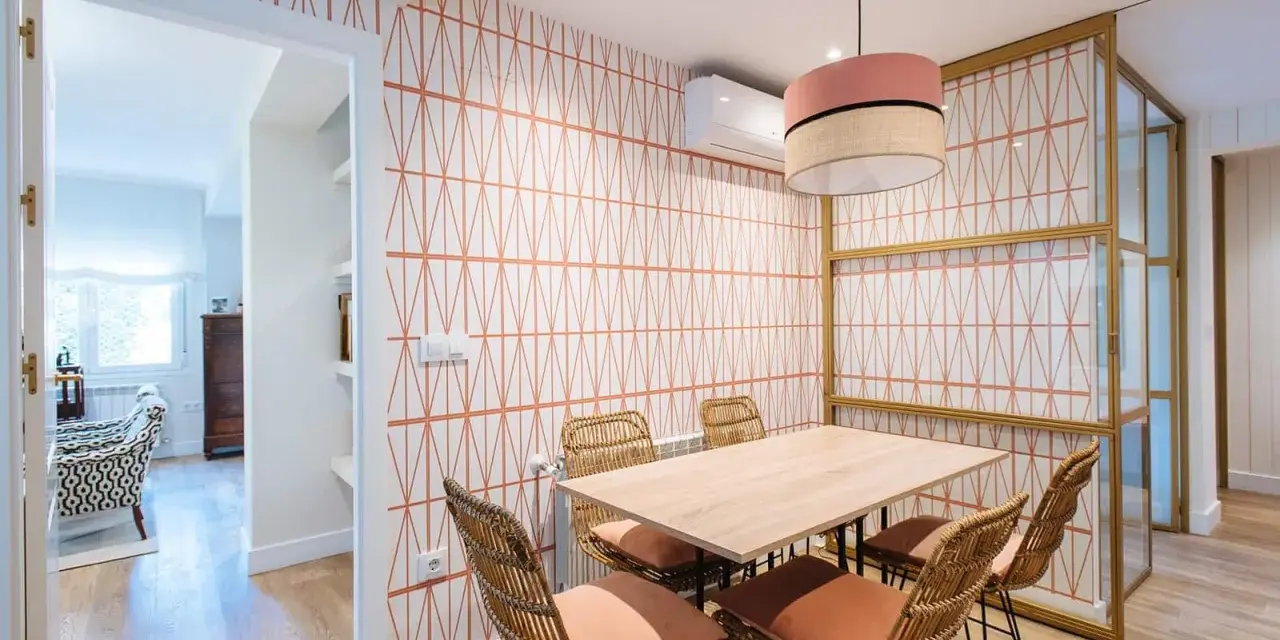 Comedor con pared empapelada con un diseño geométrico en naranja. Mesa de madera con sillas de ratán y cojines terracota.