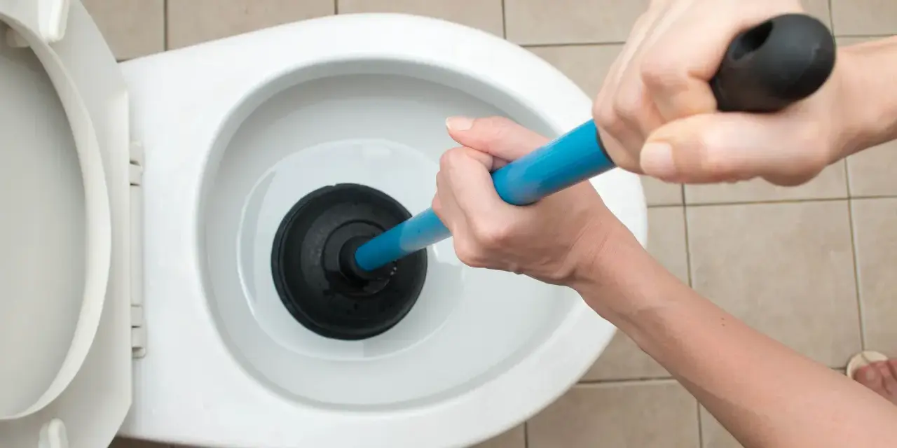 Manos usando un desatascador para como desatascar un water.