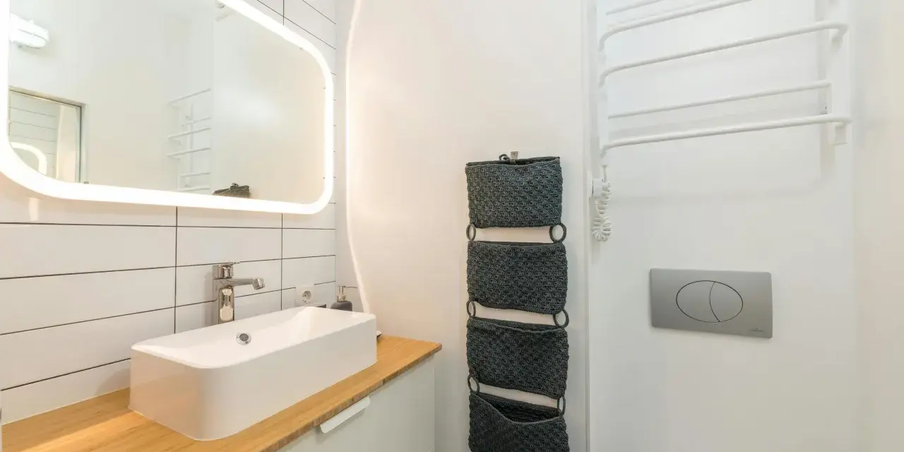 Moderno baño pequeño con lavabo sobre encimera de madera, espejo iluminado y organizadores de pared. ¡Una reforma de baño pequeño funcional y estilosa!