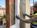 Obrero aplica mortero sobre aislamiento térmico en fachadas. El material SATE mejora la eficiencia energética.