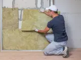 Un hombre instala aislamiento en una pared para combatir el frío en casa.