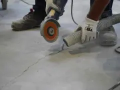 Trabajador usa una amoladora para hacer una solera de hormigón sobre tierra, aspirando el polvo.
