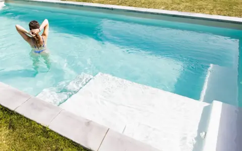 Mujer en bikini azul disfruta de una piscina cristalina, reflejo de un buen mantenimiento de piscinas.