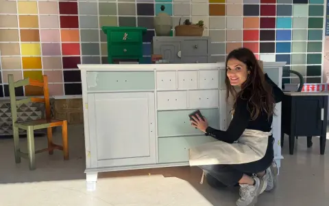 Mujer sonríe mientras trabaja en un mueble, demostrando cómo pintar muebles de madera sin lijar.