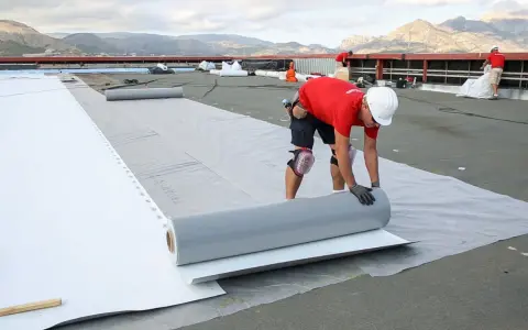 Trabajadores instalan un rollo de material para el aislante térmico exterior en una obra.
