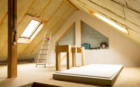 Techo interior en proceso de aislamiento. Se ve el aislante térmico para techos interiores, escalera, materiales de construcción y una ventana de tejado.