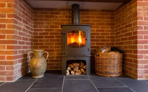 Estufa de leña con fuego encendido, chimenea de ladrillo, leña en cesta y jarrón. Guía para como instalar una estufa de leña con salida horizontal.