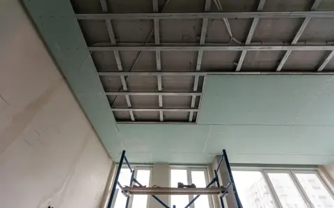 Instalación de falso techo de pladur para insonorizar habitación de ruidos de vecinos. Andamio y estructura metálica visibles.