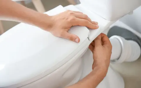 Man's hands carefully fitting the toilet seat, part of the process to como instalar un inodoro al suelo.