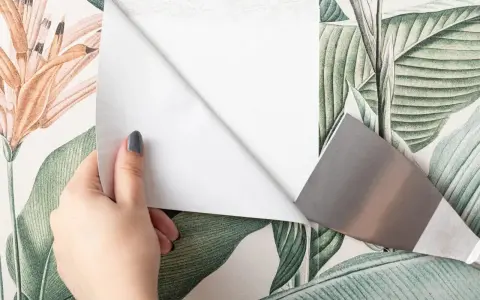 Mano quitando papel pintado floral con espátula.