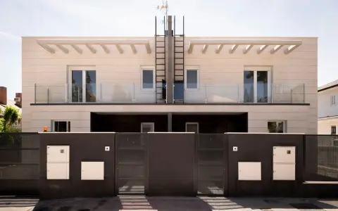 Moderna fachada ventilada de piedra clara con balcones de cristal y rejas oscuras.