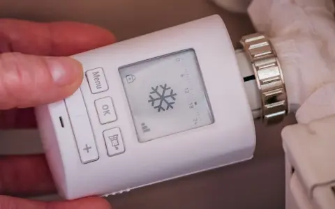 Termostato digital para sistemas de calefacción, con pantalla que muestra un copo de nieve y botones para ajustar la temperatura.