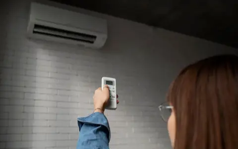 Persona ajusta control remoto de aire acondicionado, pensando en el consumo de la bomba de calor.