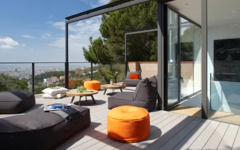 Cómoda terraza ático con sillones y pufs naranjas, vistas a la ciudad y un gran pino.