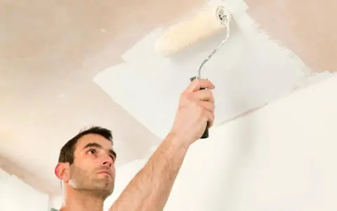 Hombre pintando el techo con rodillo. La pregunta de si que se pinta primero el techo o las paredes es clave para un buen acabado.