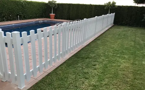Una verja de jardín blanca protege una piscina y un césped verde.