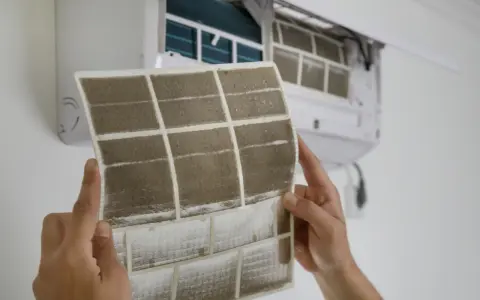 Manos sostienen un filtro de aire acondicionado sucio, mostrando cómo cambiarlo para un aire más limpio.