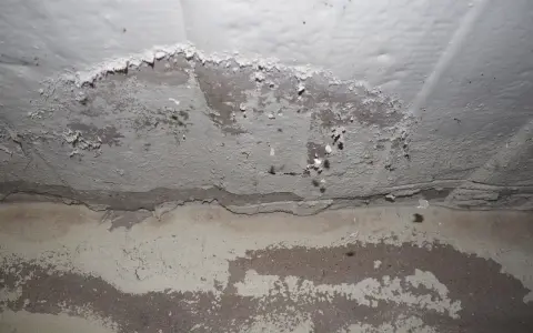 Pintura mineral descascarada en una pared, revelando capas de yeso y concreto debajo.