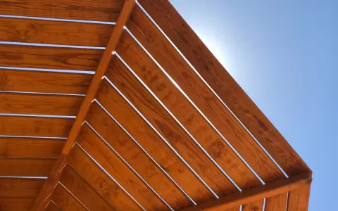 Estructura de madera con tratamiento para exterior, con lamas de madera barnizada bajo un cielo azul brillante.