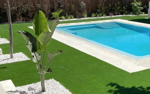 Jardín moderno con piscina y césped artificial. La colocación de césped artificial realza la belleza del espacio.