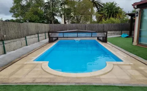 Piscina con cubierta retráctil, rodeada de césped artificial y un sistema para canalizar agua de lluvia.
