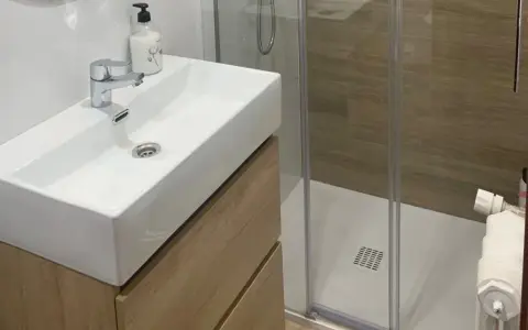 Lavabo moderno con mueble de madera y ducha acristalada. Un ejemplo de cuartos de baño modernos y funcionales.