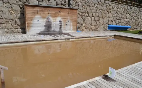 Una piscina de agua salada con un revestimiento de madera y duchas. El agua es de color marrón turbio.