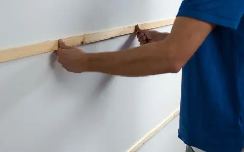Man placing wooden slats on a white wall, demonstrating como poner listones de madera en la pared.