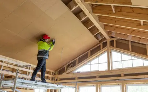Trabajador en andamio instala paneles aislantes en el techo, parte de un proyecto para como aislar una casa ya construida.
