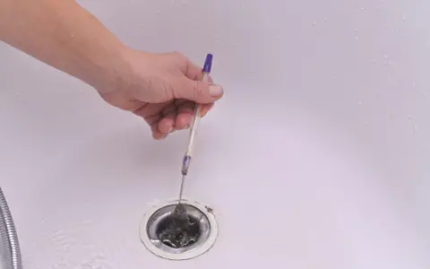 Mano usando un bolígrafo para quitar pelo y desatascar la ducha.