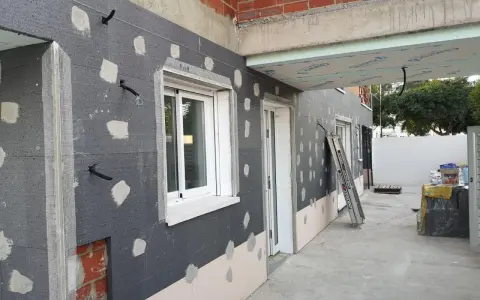 Fachada en construcción con aislamiento SATE, tuberías y ventanas.