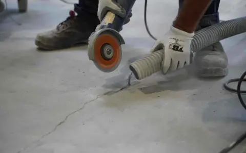 Trabajador usa una amoladora para hacer una solera de hormigón sobre tierra, aspirando el polvo.