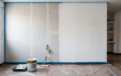 Preparativos para pintar pladur: cinta azul protege el suelo y la pared, cubos de pintura y rodillo listos para transformar la estancia.