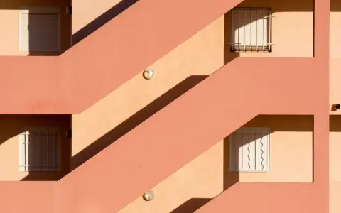 Fachada con escaleras y ventanas, sombras marcadas. Un ejemplo de cómo impermeabilizar pared exterior para protegerla.