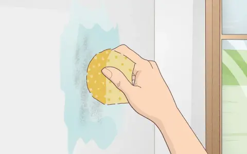 Mano limpiando una mancha en pared blanca con esponja y agua. Aprende como limpiar paredes blancas fácilmente.